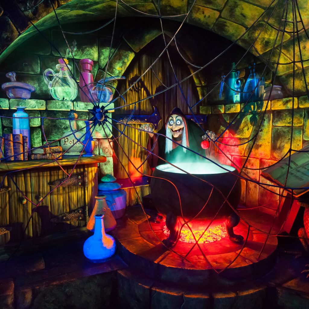 The Queen in disguise holding an apple beside a glowing cauldron inside Blanche-Neige et les Sept Nains
