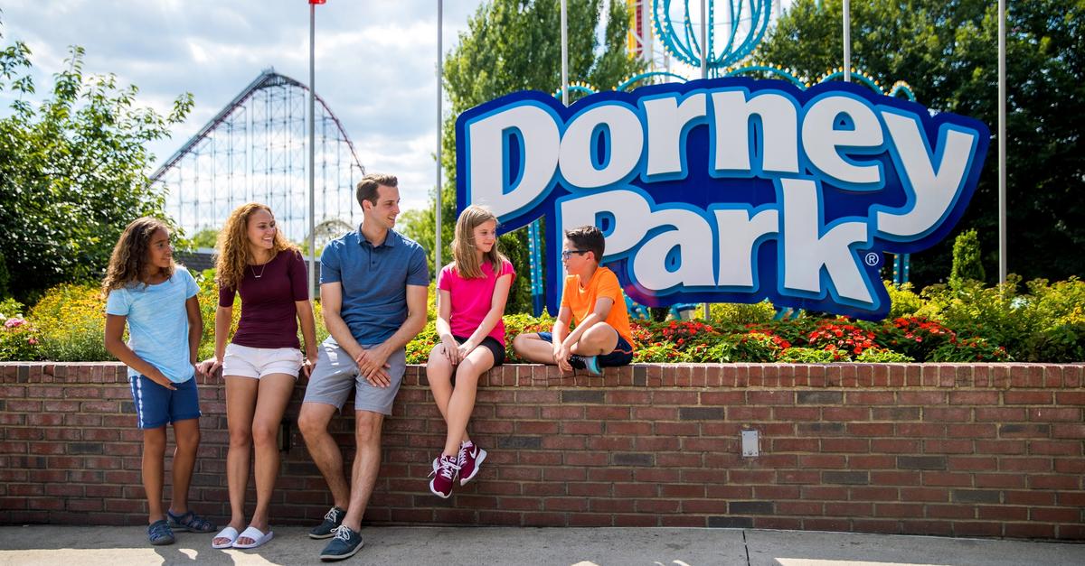 Family sitting by the Dorney Park entrance sign with a coaster in the background