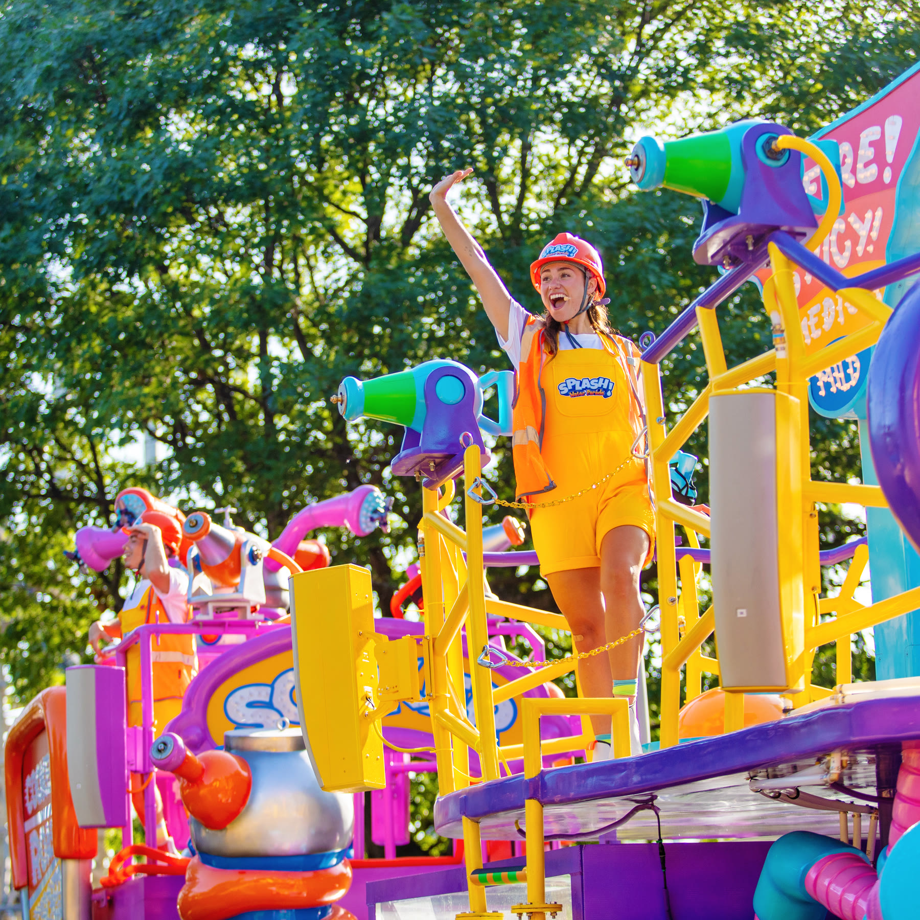 A SPLASH! Water Parade performer waves from a float fitted with water cannons
