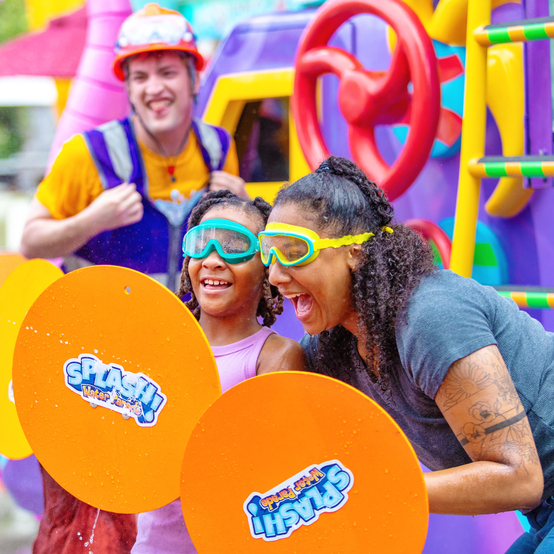 A child and adult wear goggles behind orange SPLASH! Water Parade shields