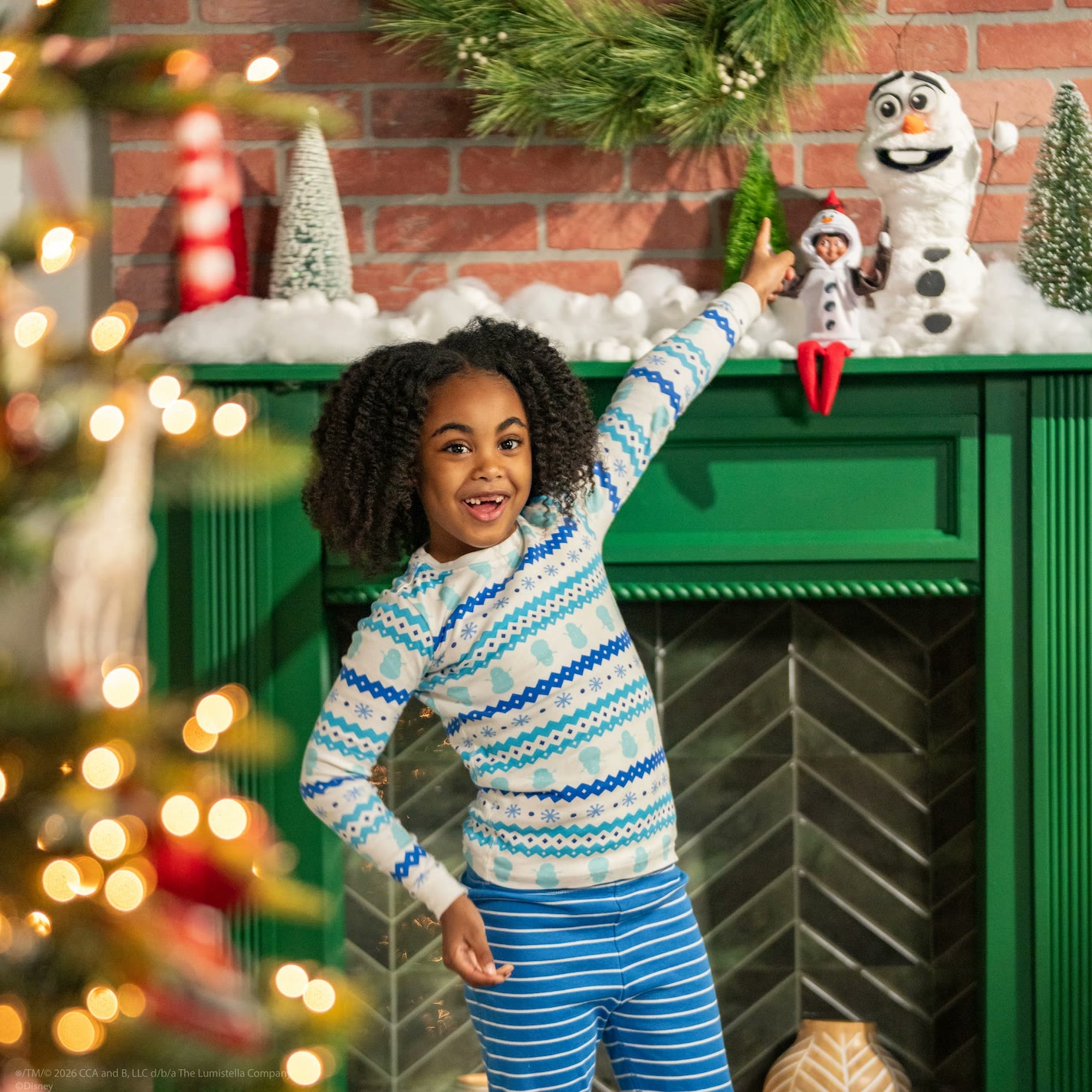 Child points to an Elf on the Shelf wearing Olaf accessories in a snowy display
