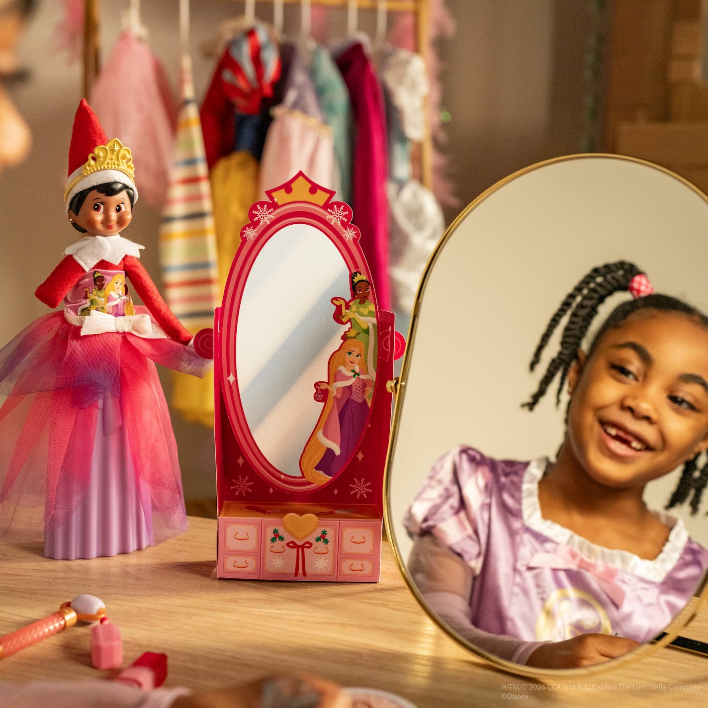 A child and an Elf on the Shelf pose with Disney Princess dress-up accessories