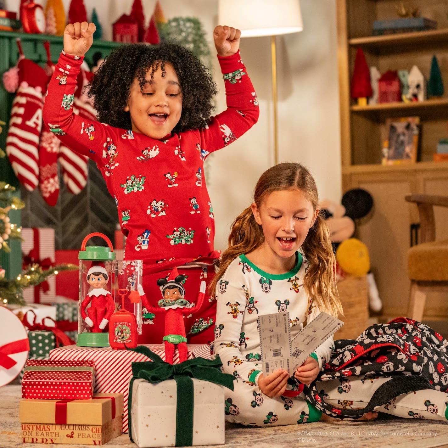 Two children hold travel tickets near an Elf on the Shelf and a miniature suitcase