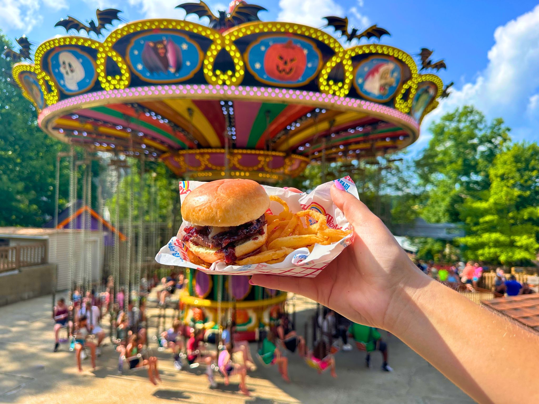 Festival burger and fries held in front of a Holiday World swing ride