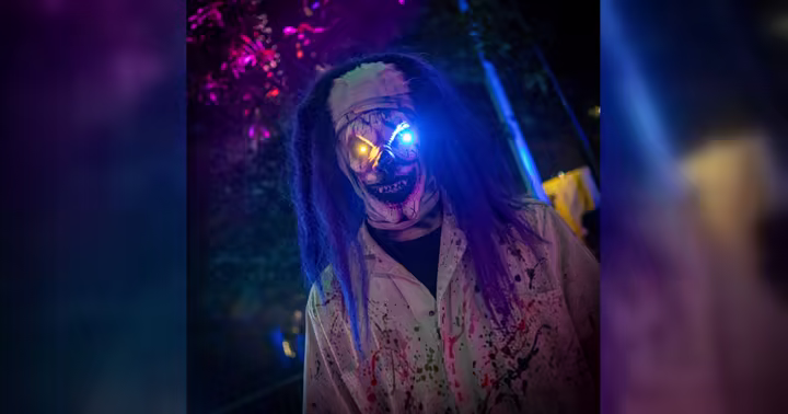 A Dorney Park Halloween Haunt character in a purple and blue-lit wooded setting