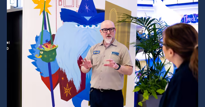 Disneyland Resort artist Brett standing beside Monsters, Inc. Halloween artwork at Pixar Place Hotel