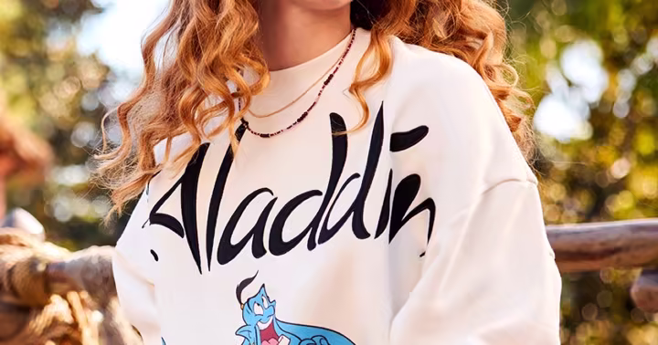Model wearing a cream Aladdin sweatshirt with Genie, Jasmine, Aladdin and Jafar artwork