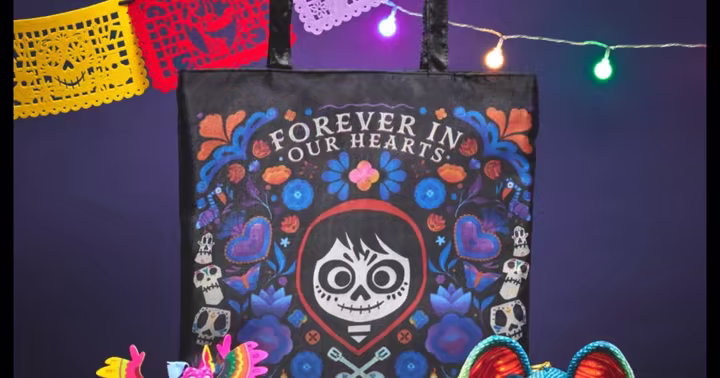 A Coco tote bag displayed with colorful alebrije figures, papel picado and string lights