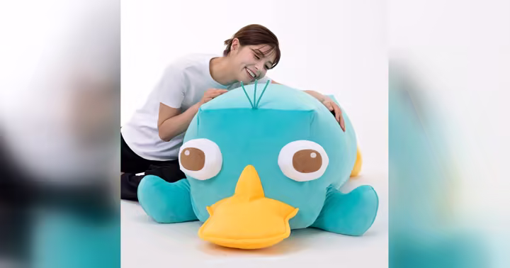 A person leaning over a super-sized Perry the Platypus plush
