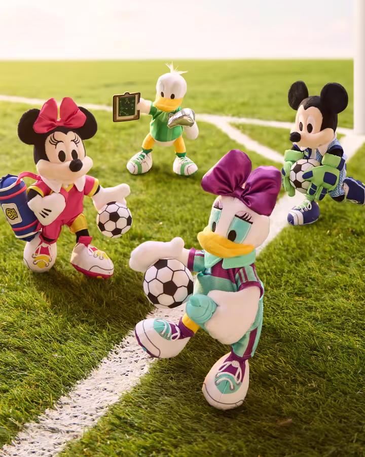 Minnie, Daisy, Donald, and Mickey soccer plushes on a soccer field
