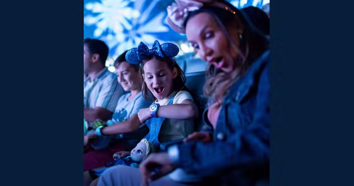 A child looks at a MagicBand on her wrist while seated with her family at Walt Disney World