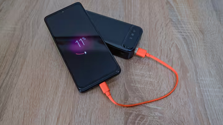 A smartphone connected to a portable power bank with an orange charging cable