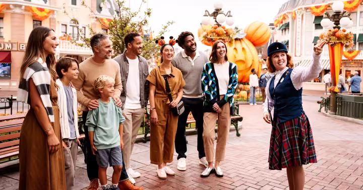 A Disneyland tour guide holding a lantern with Halloween-costumed guests on Main Street, U.S.A.
