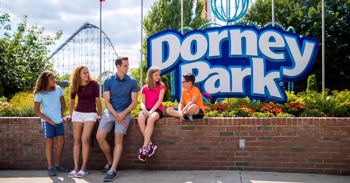 Family sitting by the Dorney Park entrance sign with a coaster in the background