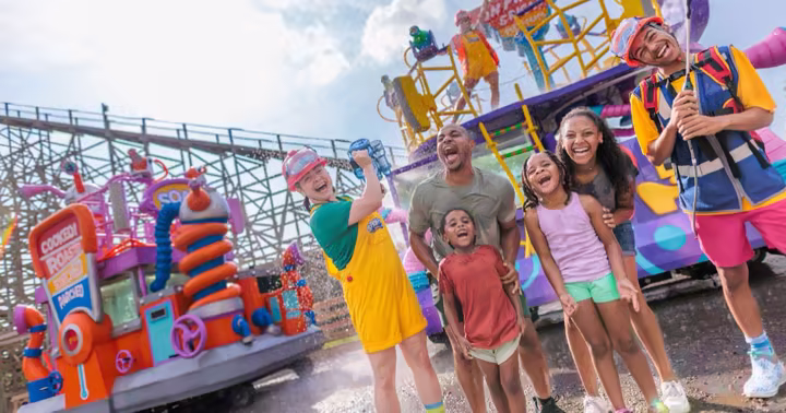 Families and SPLASH! Water Parade performers stand beside a water-spraying float at Dorney Park
