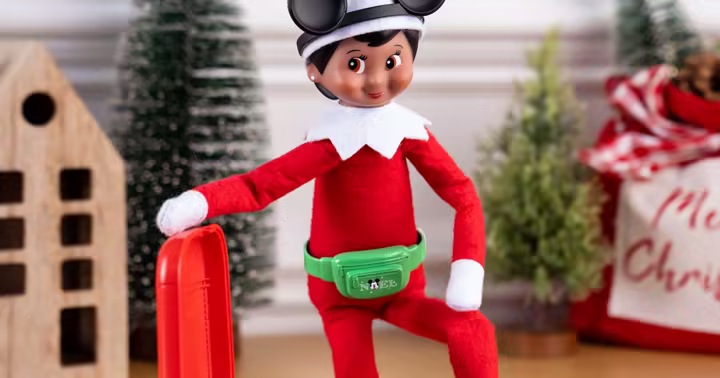 Elf on the Shelf wearing Mickey Mouse ears beside a red suitcase