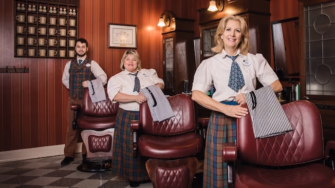 Three barbers standing beside the chairs inside Harmony Barber Shop at Magic Kingdom