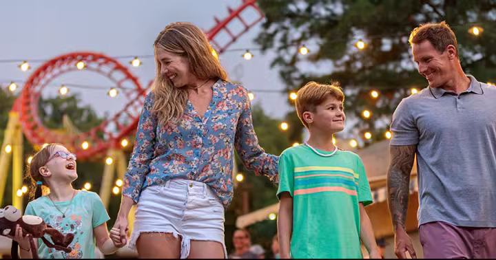 Family walking beneath the lights at Kings Island with a red roller coaster behind them