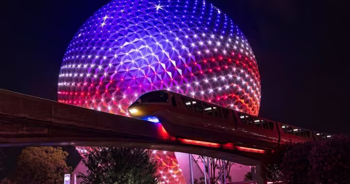 Spaceship Earth illuminated behind the EPCOT monorail at night