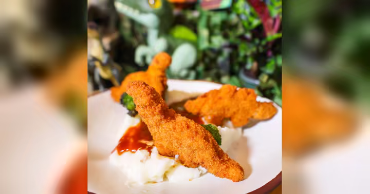 Dinosaur-shaped chicken nuggets on mashed potatoes with barbecue sauce and broccoli