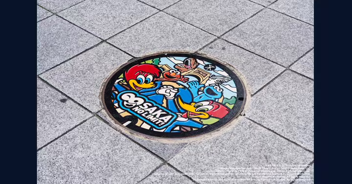 USJ anniversary manhole cover with Woody Woodpecker, Sesame Street characters, Jaws, and Jurassic Park dinosaurs
