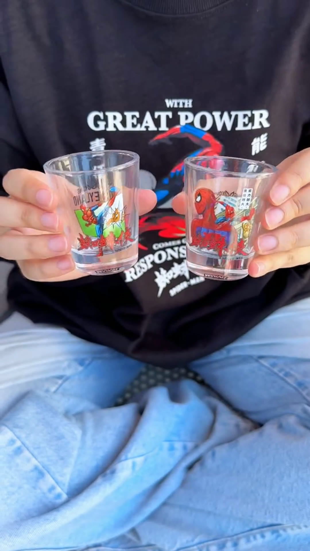 Two Spider-Man drinking glasses held in front of a black Spider-Man graphic T-shirt