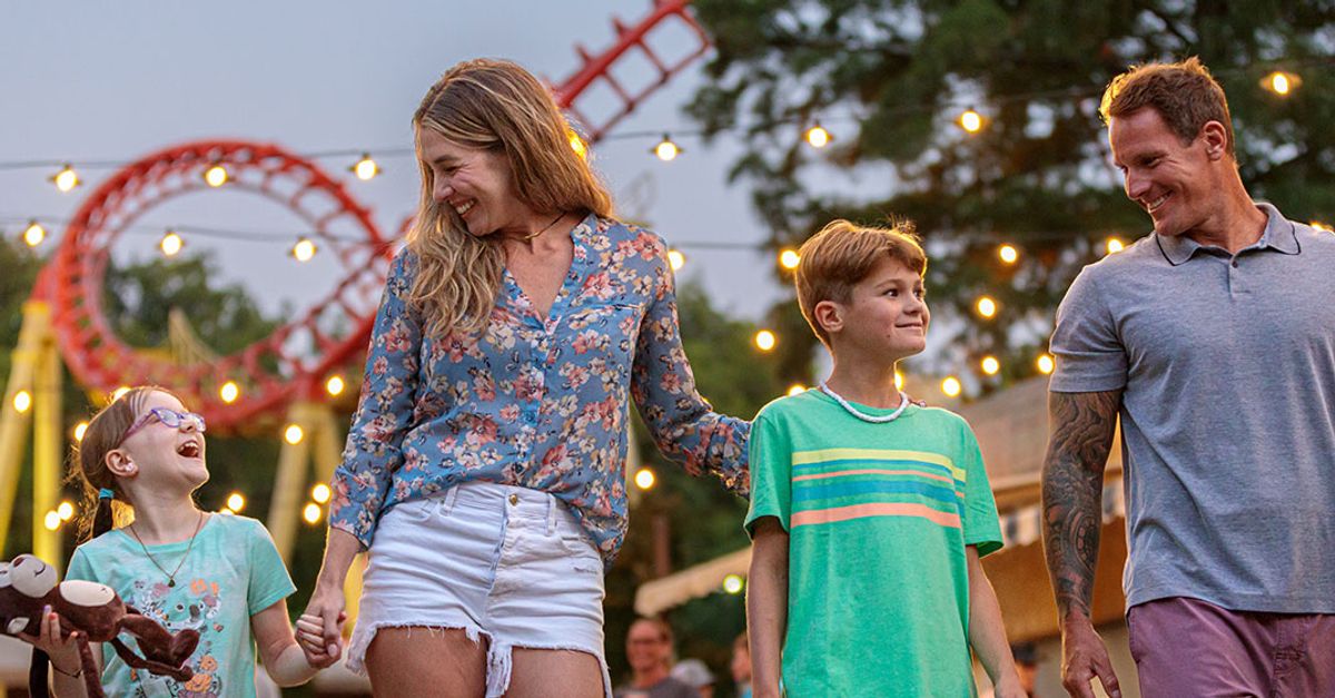 Family walking beneath the lights at Kings Island with a red roller coaster behind them