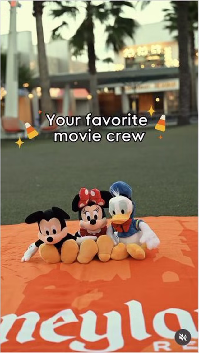 Mickey Mouse, Minnie Mouse and Donald Duck plush sit on an orange Disneyland Resort blanket at Downtown Disney