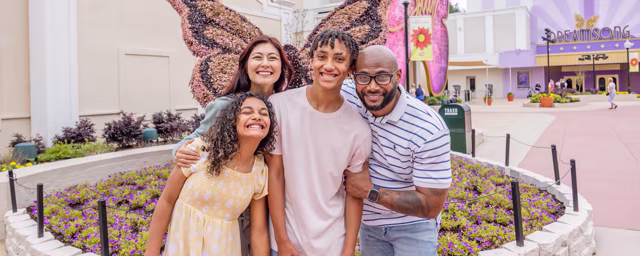 A family poses at Dollywood with the floral butterfly display and Dreamsong Theater behind them
