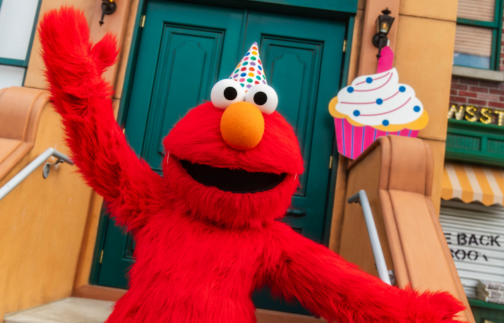 Elmo wears a party hat beside birthday balloons