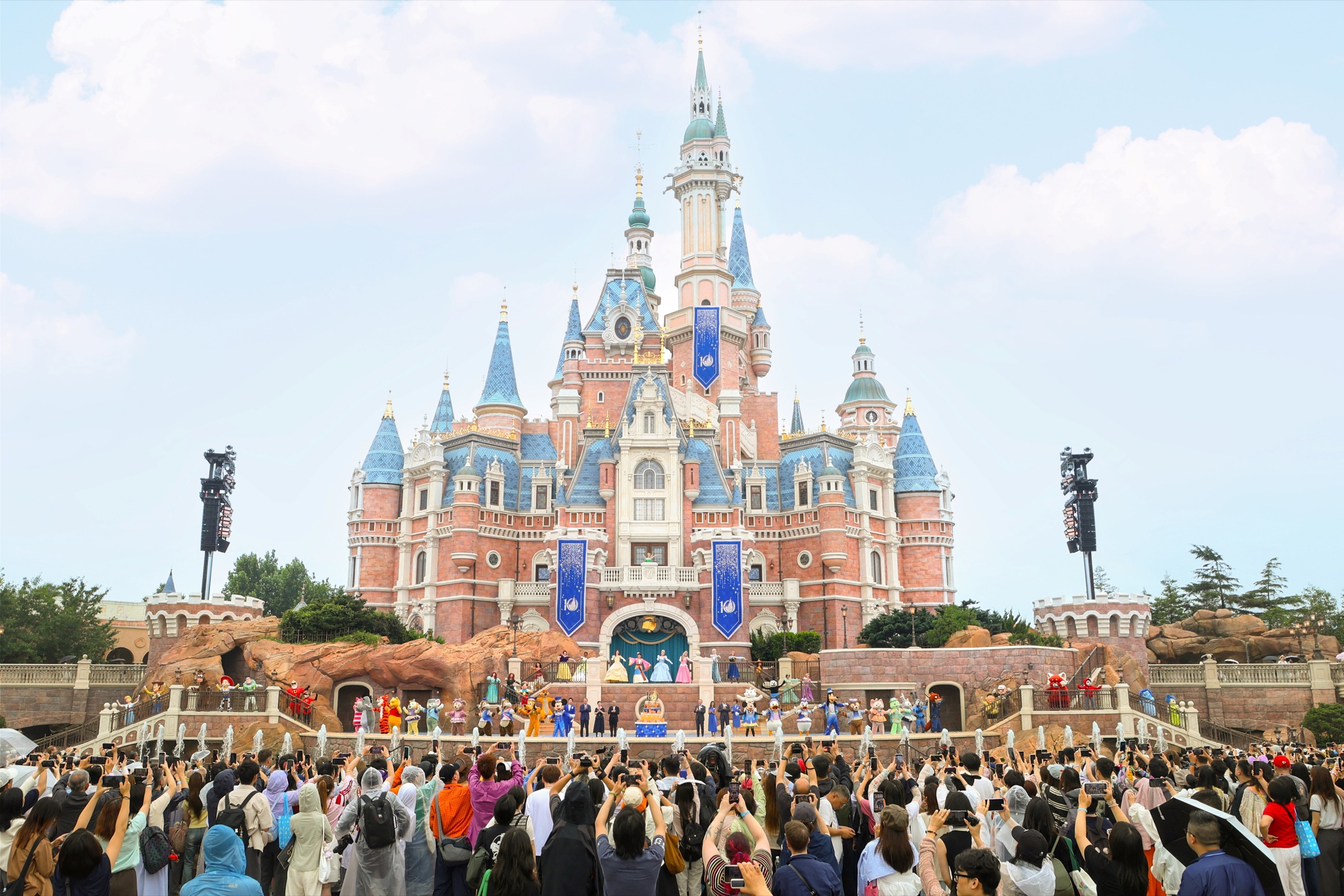 Disney characters and performers gather around Shanghai Disney Resort's 10th birthday cake in front of Enchanted Storybook Castle
