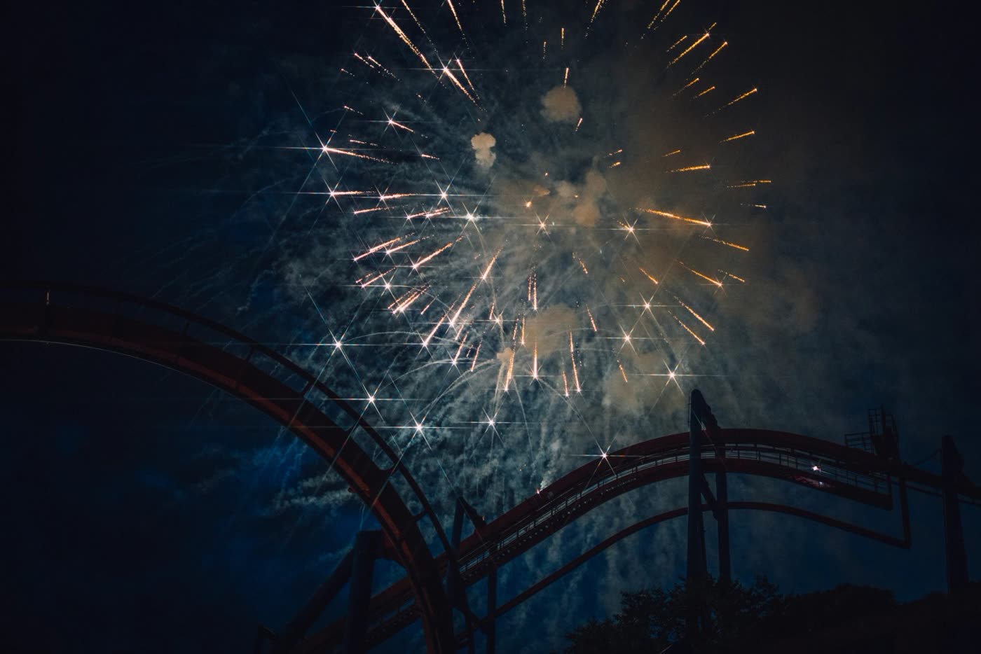 Fireworks burst above a roller coaster track at night