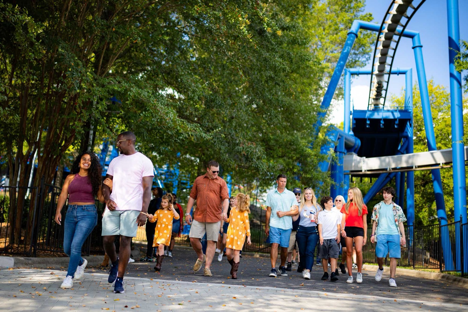 Guests walk past a blue roller coaster at a Six Flags park