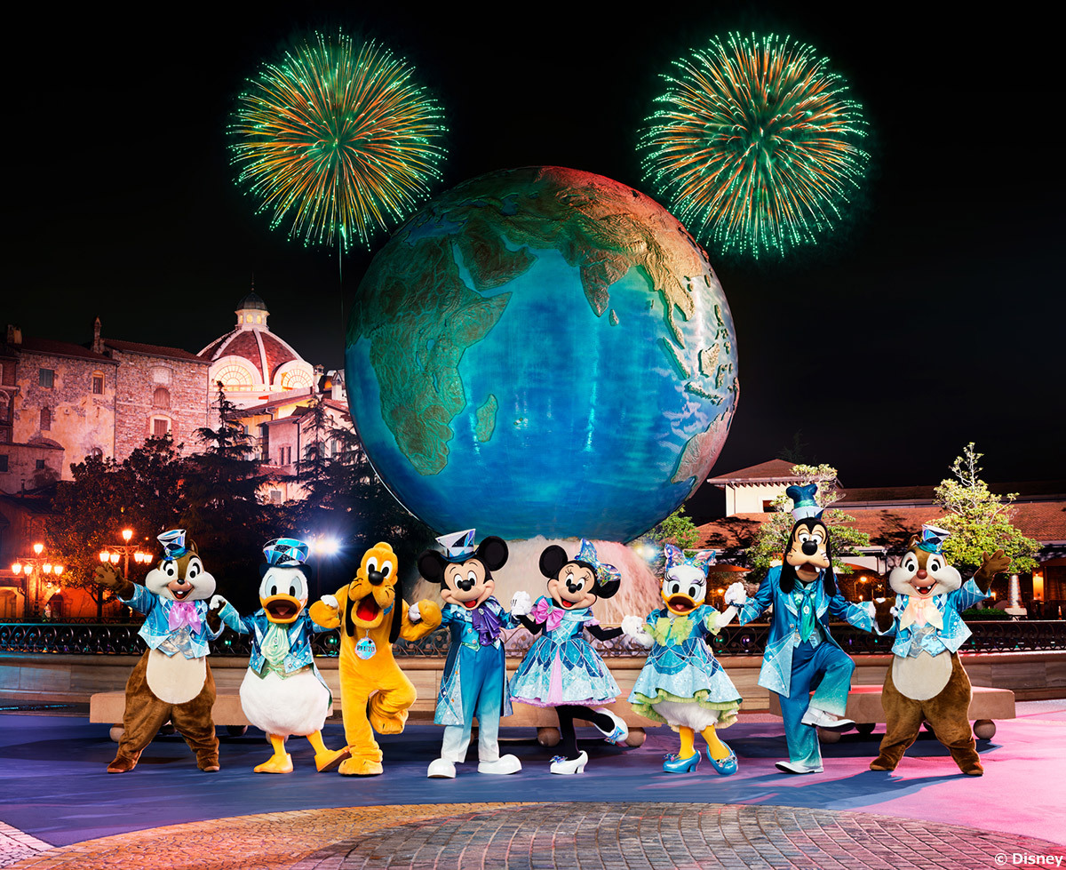 Mickey Mouse and friends posing in front of the Tokyo DisneySea Aquasphere and green fireworks
