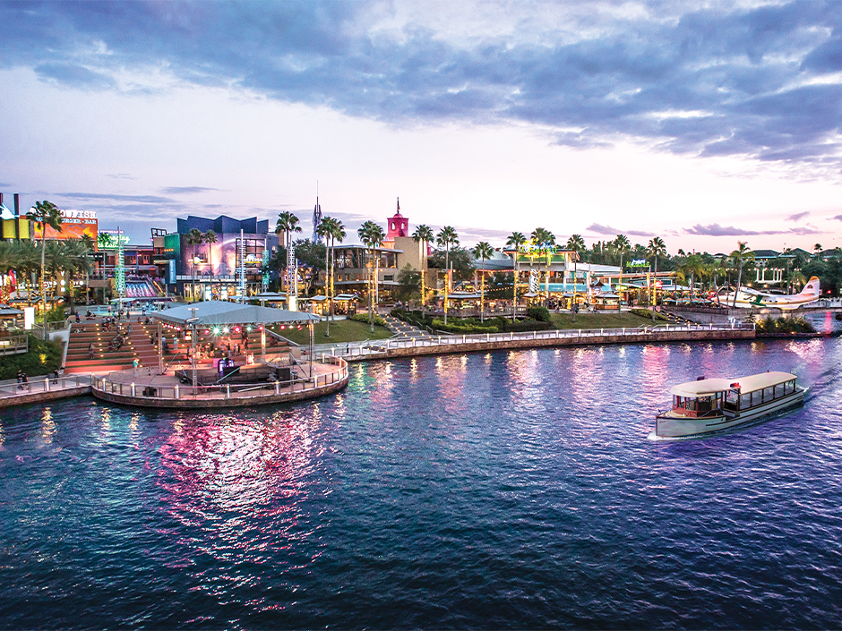 Universal CityWalk at dusk, viewed across the lagoon with a water taxi in the foreground