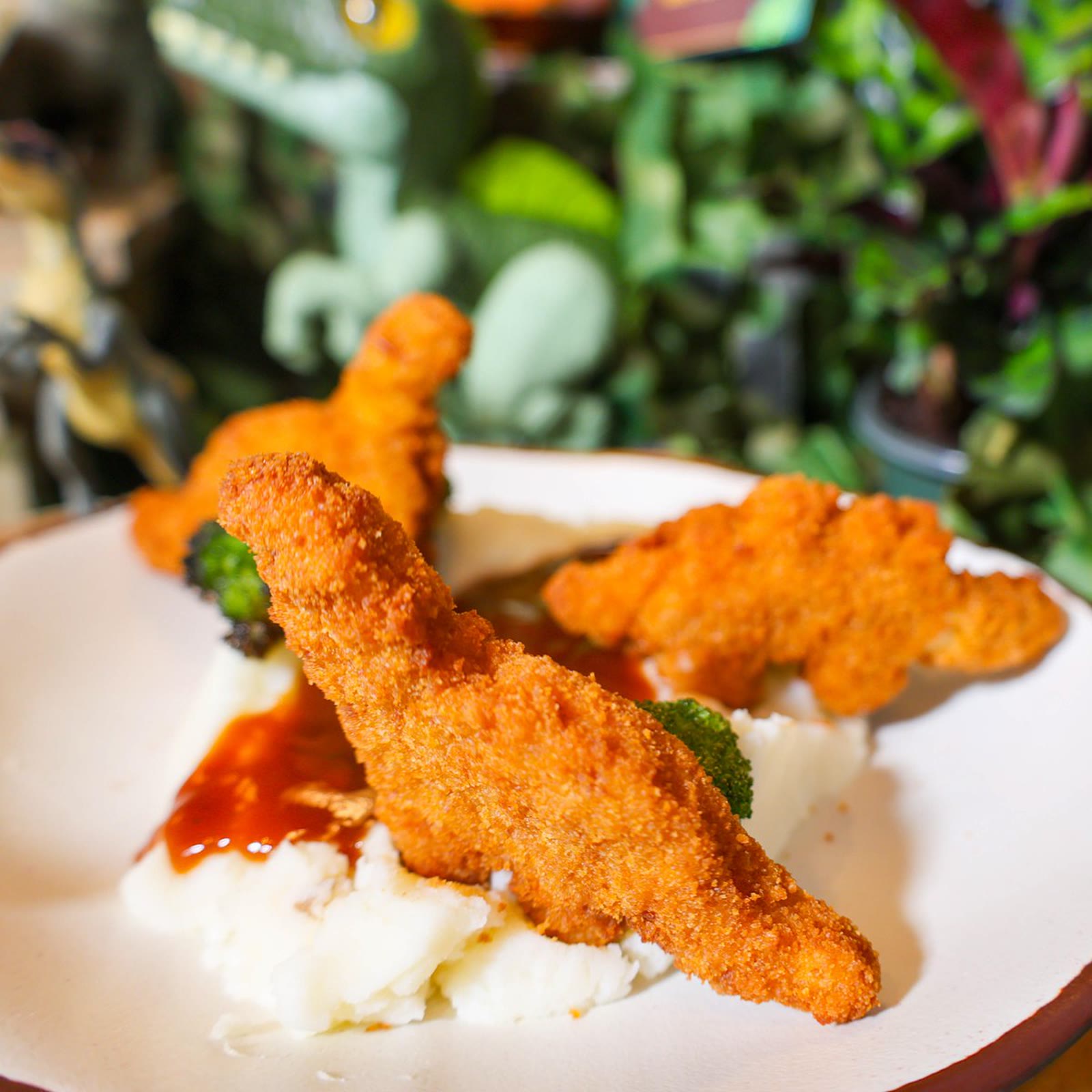 Dinosaur-shaped chicken nuggets on mashed potatoes with barbecue sauce and broccoli