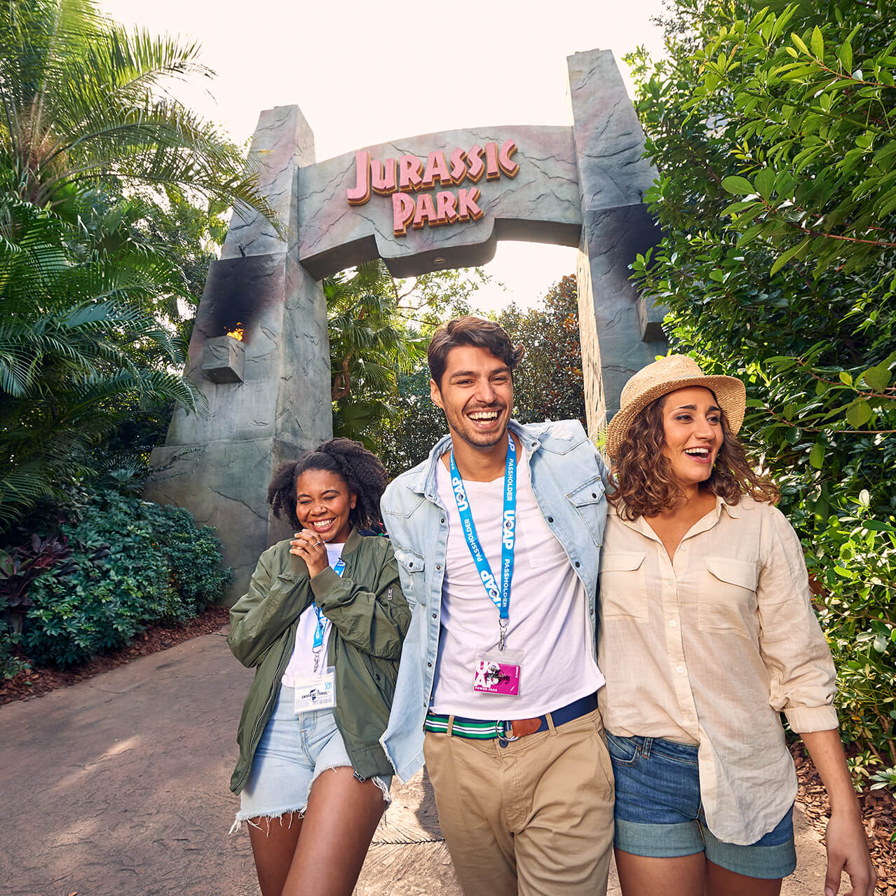 Three Universal Orlando Passholders smiling beneath the Jurassic Park entrance