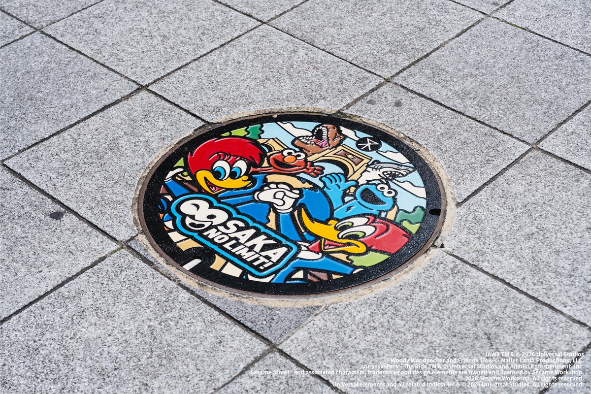 USJ anniversary manhole cover with Woody Woodpecker, Sesame Street characters, Jaws, and Jurassic Park dinosaurs