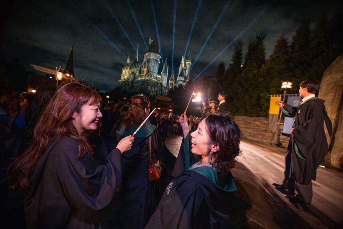 Guests raise wands as Hogwarts Castle glows during Universal Studios Japan's Back to Hogwarts event