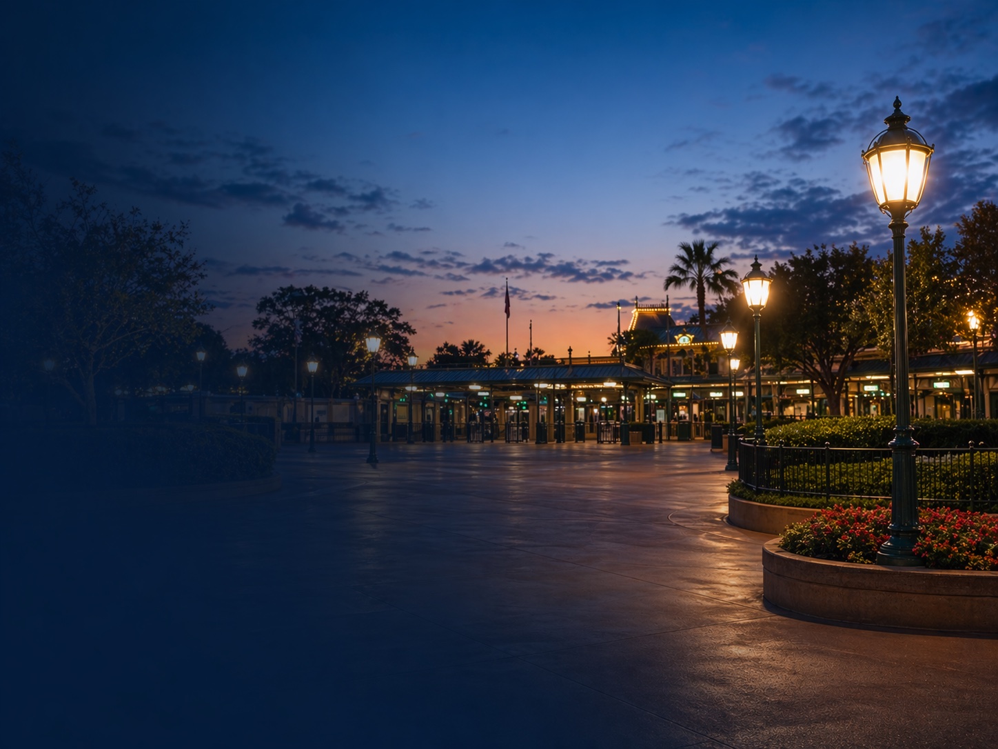 Theme park entrance area with glowing lamps at dusk and an open plaza